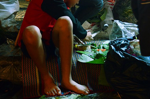 A boy cuts banana leaves that are then used to decorate and wrap the 'krathongs'. 'Krathongs' are usually made of banana tree trunk and decorated with candles and various flowers and plants. With the volume of tourists and locals during Loi Krathong, both young and old line the streets and riverbank with stalls that make and sell these floating baskets.