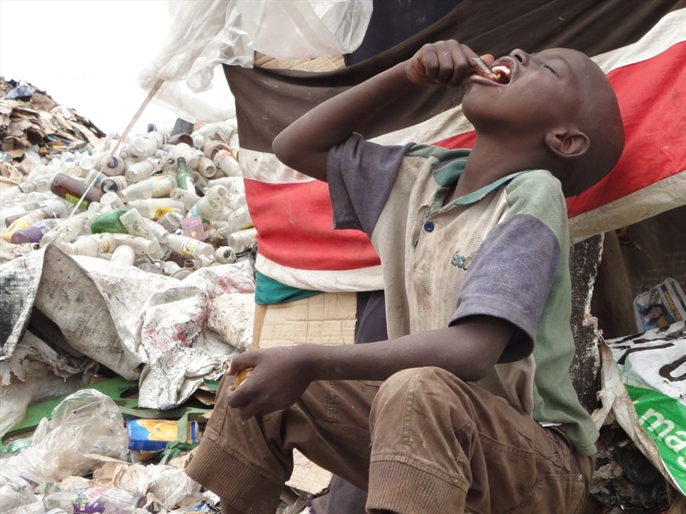 After along day of searching for plastics and scraps under the scorching sun the boy enjoys  his meal beside a shelter they had made with his group.
