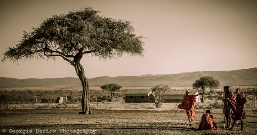 Some Maasai tribesmen catch up near a tree overlooking the Maasai Mara, Kenya