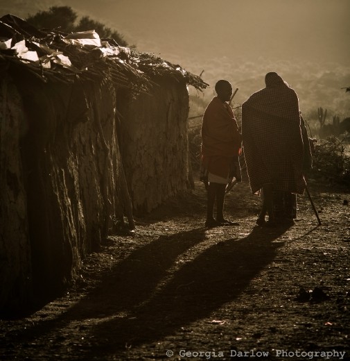 A couple of Maasai tribesmen stand chatting at dusk.