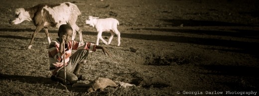A boy helps keep watch over his herd with a loyal puppy at his feet in the Maasai Mara, Kenya