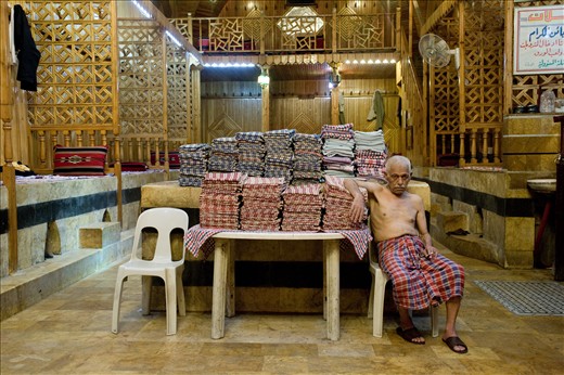 After a long day of tending to clients in the Al Nahaseen Hammam inside the souk, this gentleman relaxes next to a pile of clean towels. Today, news photos show the hammam being used as a rebel base.