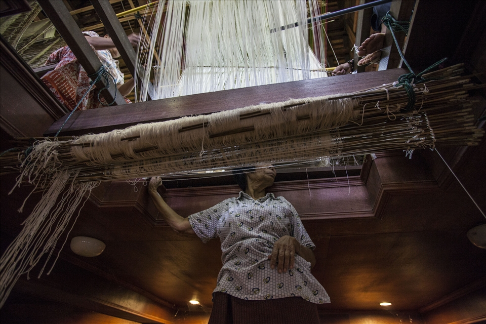 The process in Ban Thasawang, a village weaving silk for the elites, is much more complicated than on the semi-automatic loom.  It requires four to five people working together on one piece of fabric. Even though they work as a team, one person always sits below the ground level. Immersed in semidarkness and isolated from the gossips above, staring blankly ahead.  This figure is perhaps the best metaphor for the state of the nation's homegrown industry.