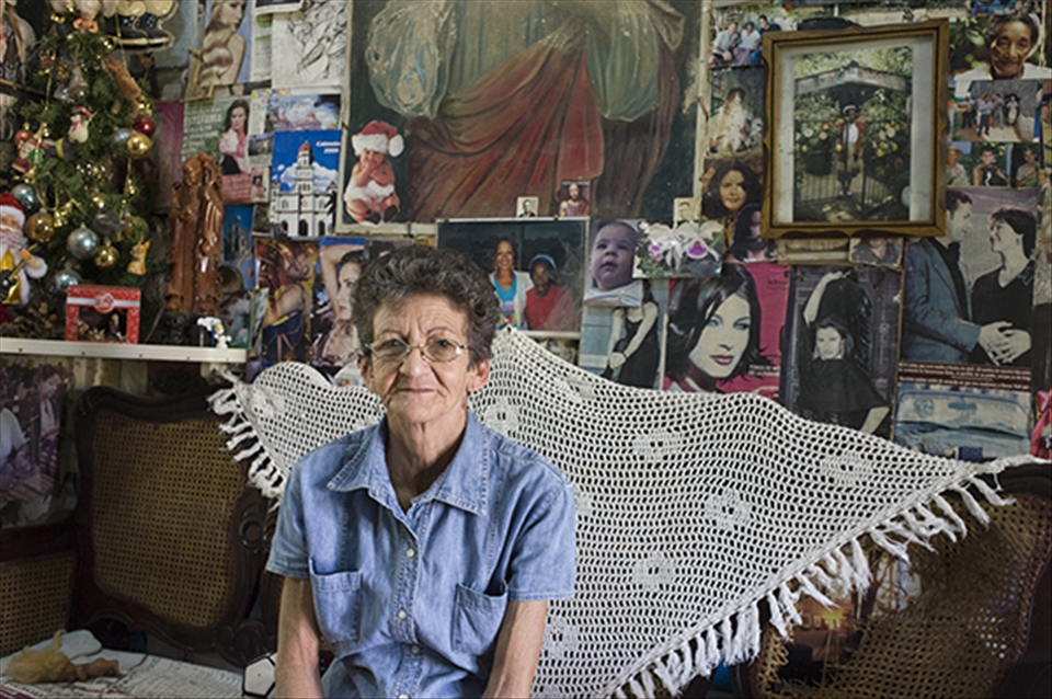 It is common for three generations to be sharing a roof in Cuba. This grandmother is in her living room with treasured memories on the wall, Viñales. 
