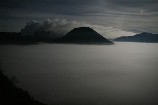 Lit only by moonlight, the view from Cemoro Lawang on the edge of the Tengger Caldera shows the Sea of Sand (Segara Wedi) covered by fog at 4:30am. Mt Bromo can be seen steaming to the left while the majestic Mt Batok is to the right. The early start is to enable us to get to view the sunrise over the Tengger Caldera, a 45 minute trip in a 4-wheel drive down into the caldera, across the Sea of Sand and up Mt Pananjakan on a different side of the caldera to the usual viewing location.