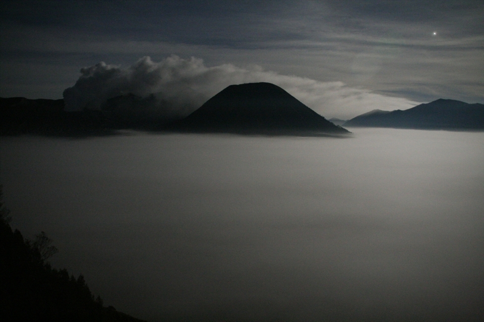 Lit only by moonlight, the view from Cemoro Lawang on the edge of the Tengger Caldera shows the Sea of Sand (Segara Wedi) covered by fog at 4:30am. Mt Bromo can be seen steaming to the left while the majestic Mt Batok is to the right. The early start is to enable us to get to view the sunrise over the Tengger Caldera, a 45 minute trip in a 4-wheel drive down into the caldera, across the Sea of Sand and up Mt Pananjakan on a different side of the caldera to the usual viewing location.