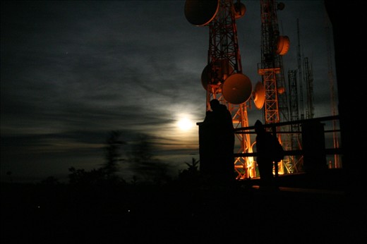 Waiting for sunrise on Mt Pananjakan, late arriving tourists try to obtain better viewing positions by climbing onto the communications building under the illumination of moonlight and security lights. Viewing the sunrise from this location is one of the main attractions of the Bromo Tengger Semeru National Park and the tourists are four deep around the edge of the platform.
