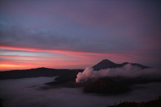 Sunrise over Bromo Tengger Semeru National Park. To the left Mt Bromo steams in the early morning cold air while Mt Batok, the only non active volcano in the park, is the perfect volcano cone in the foreground. In the distance the highest peak on Java, Mt Semeru, can be seen.