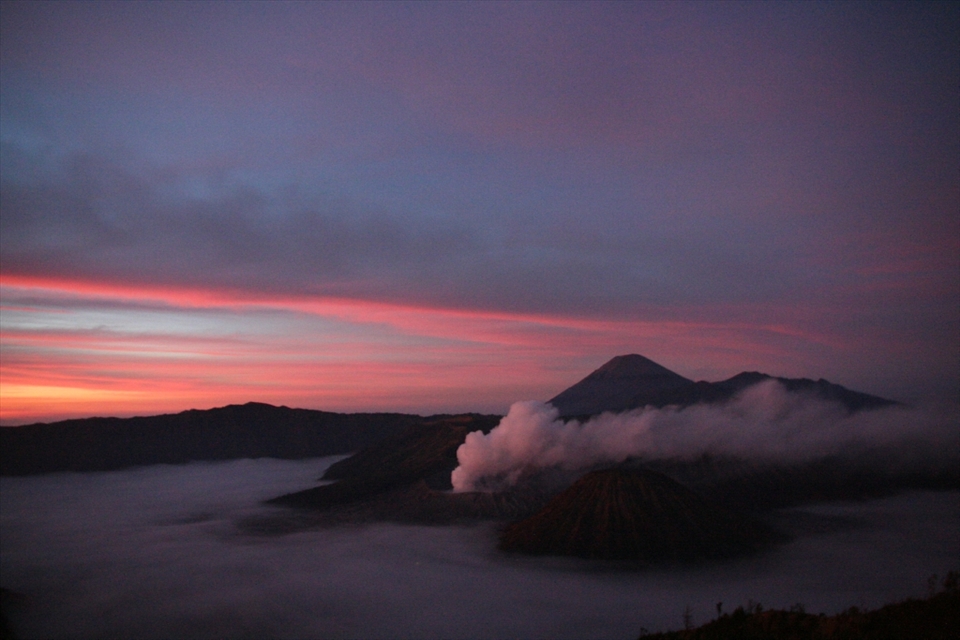 Sunrise over Bromo Tengger Semeru National Park. To the left Mt Bromo steams in the early morning cold air while Mt Batok, the only non active volcano in the park, is the perfect volcano cone in the foreground. In the distance the highest peak on Java, Mt Semeru, can be seen.