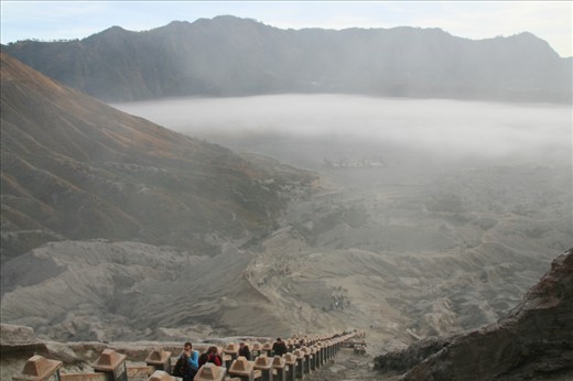 View through the morning mist from the top of the staircase up Mt Bromo to the Hindu temple Pura Luhur Poten on the Sea of Sand beside Mt Batok. Tourists on their morning sunrise tour finish the trip by climbing up from the temple, the smell of sulphur getting stronger as they near the top of the mountain.