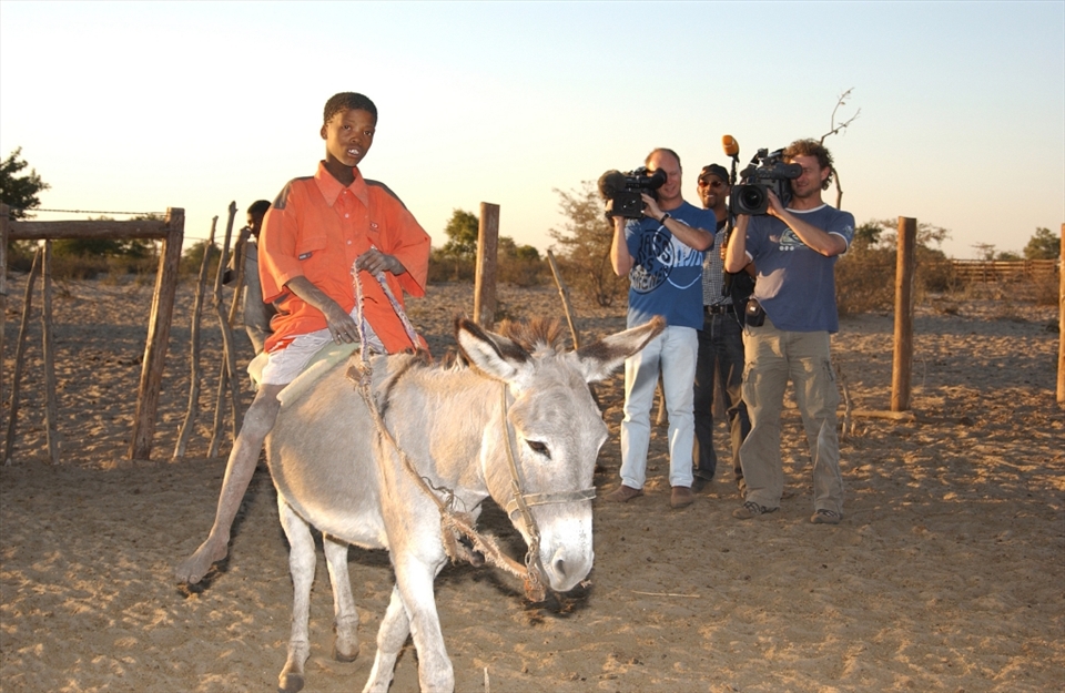 A film crew shooting a Bushmen boy riding their common mode of transport, donkey. 