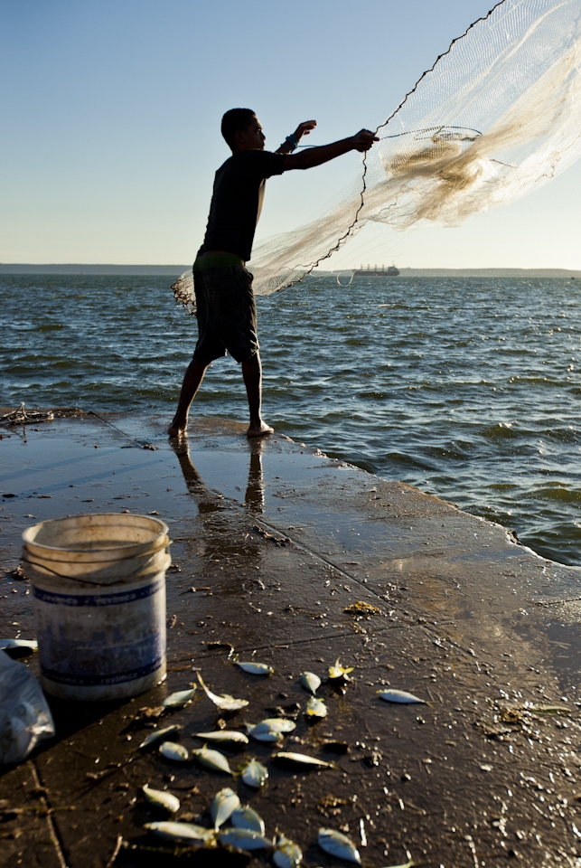 A young fisherman casts his net made of intertwined fishing line and rope.