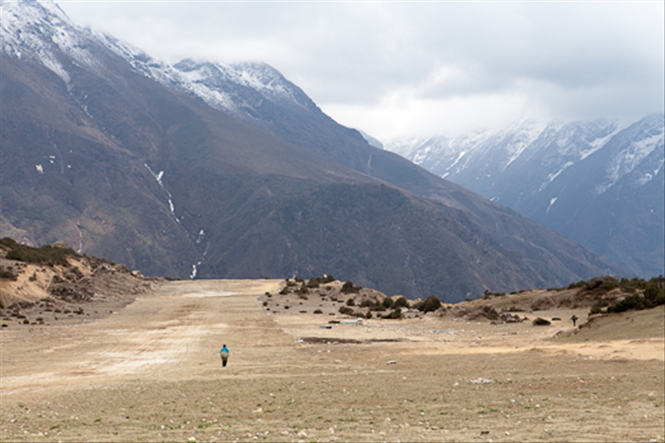 The Long Walk Home.  Captured at the highest airstrip on earth.  Approximately 12,200 feet above sea level, the little dirt track at Syangboche services the largest village in the Everest region, Namche Bazaar.  A lone porter, most likely ferrying supplies between mountain villages and walking ten plus hours a day, stands alone amongst the vast wilderness at the top of the world. 