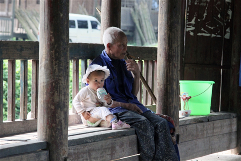 A grandfather & his granddaughter are resting in the shade of one of Dimen's bridges.

These impressively colourful constructions cater for the community as a meeting space, shade and to connect the different parts of the village that embrace the river running through it.