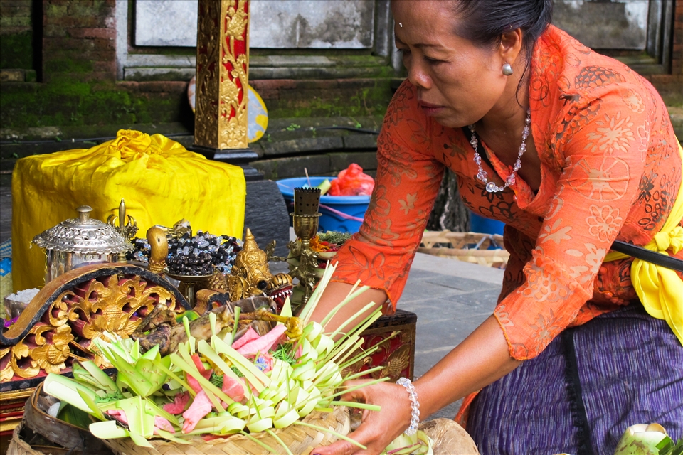 A woman dressed in traditional clothing is preparing 'Sampian' made from young white coconut leaf called 'Busung' which have sacred meaning for religious ceremony. 'Sampian' is carefully put and crafted to be presented to God.