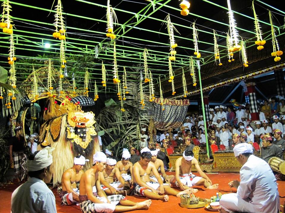 A part of Hindu religion ceremony held religiously with Barong (a sacred good spirit creature) stands behind, men with their heads down sit in front of the leader to receive prayers as a symbol of fighting the devil. Everyone else who come stand at its surrounding to watch how it happens.