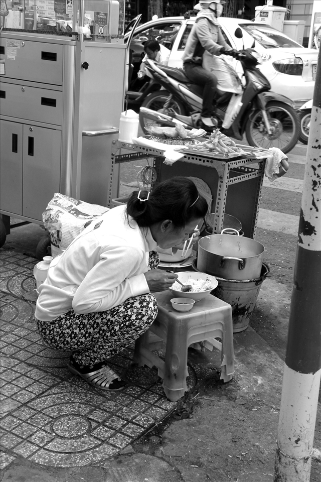 A woman trying to finish her simple meal right next to the crowded dusty street 