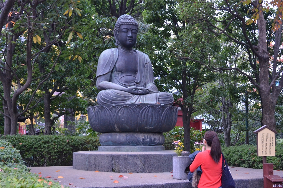 Even in the midst of the busy Tokyo district of Asakusa, one can still find peace and serenity. As seen here, a passer-by stops to pay her respects to Buddha in the quiet garden of Sensoji.