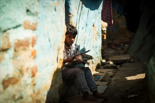 A boy does his school homework outside his house in a slum