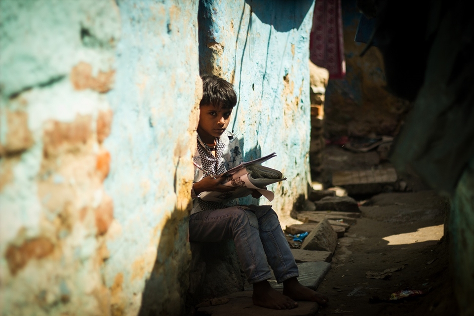 A boy does his school homework outside his house in a slum
