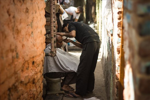 A man gets a shave in a tight lane of a slum