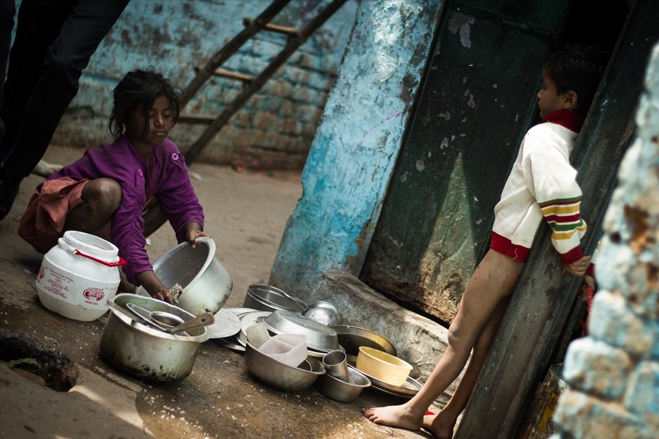A boy looking at her sister washing utensils in a slum area