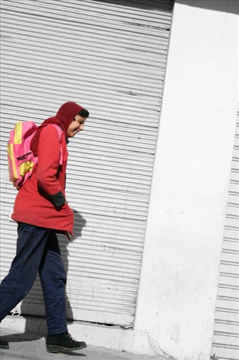 A boy is walking home from school all by him self, smiling. 