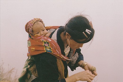 Along the muddy, wintery trek, a mother with her baby safely bundled in fabric, stops to collect dry grass and wrap it around her hand. 