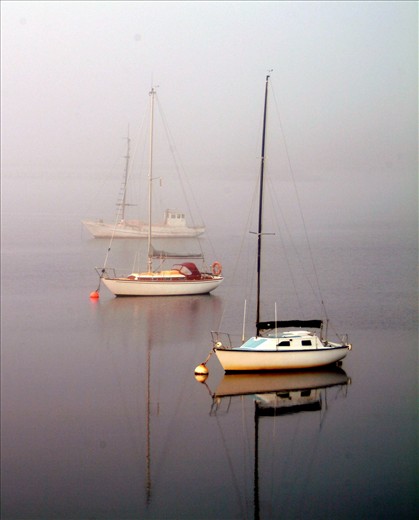 Early morning as the fog slowly lifts and three lonely boats dot the water.