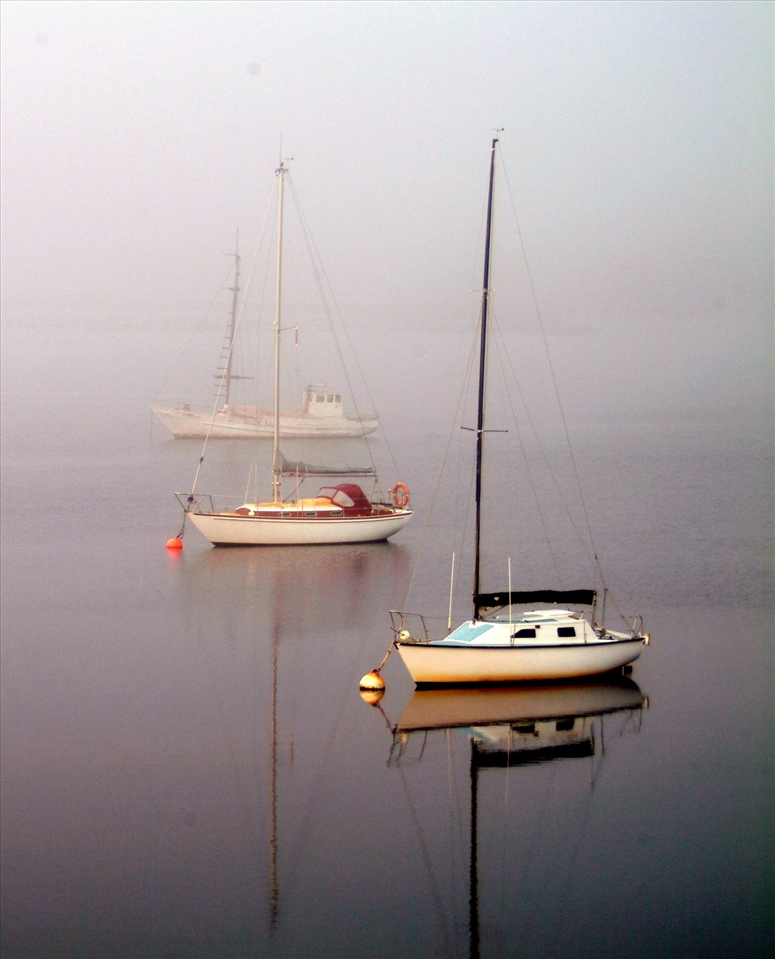 Early morning as the fog slowly lifts and three lonely boats dot the water.