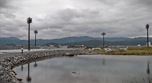 Opposite one of the only remaining buildings still standing in this area (a 6 story hotel where nothing remains except an empty shell from the 5th story down, showing just how high the wave was) was a space where a baseball pitch used to be. It was very quiet here, very calm. A flock of birds flew by just after I took this photo and together with the still floodwater and rolling hills almost made the scene seem peaceful. The harsh reminder of reality comes in the form of four floodlights, standing like lonely sentinels, the only notable thing that pierces the now desolate horizon.