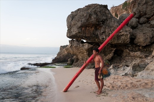 This fisherman was waiting for the right moment to head out to the sea to set up fish traps. The long red pole would be used as a floatation as he swims out.