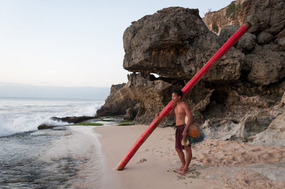 This fisherman was waiting for the right moment to head out to the sea to set up fish traps. The long red pole would be used as a floatation as he swims out.