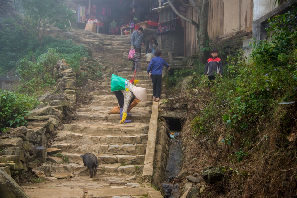 Village children welcoming visitors as a little piglet runs up the stairs.