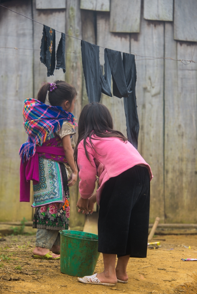 Two young H'mong girls hanging clothes to dry outside their house. 