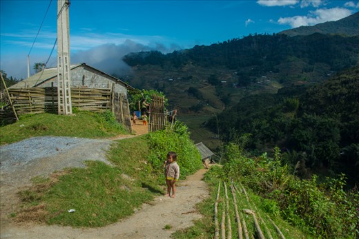 A little girl seems bewildered as she stands outside her house atop a hill.