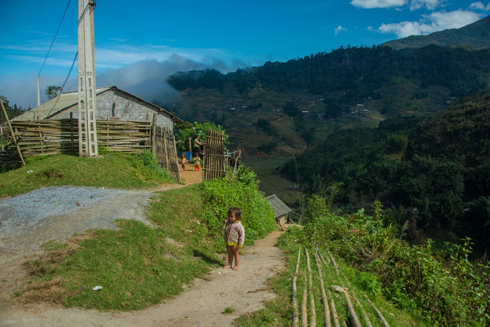 A little girl seems bewildered as she stands outside her house atop a hill.