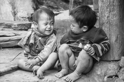 Two little boys, not wearing any pants, playing outside of their house. 