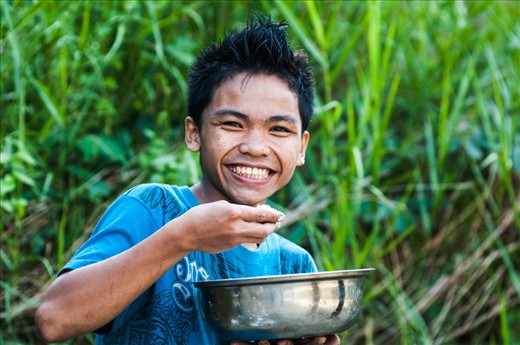 A boy smiling at me while having his lunch at the river.
