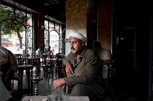 A portrait of a local man who dressed in the traditional Egyptian clothes. he was sitting in a coffe shop at the early morning to have breakfast and smoke some shisha, while other people chatting together at the background(left)
