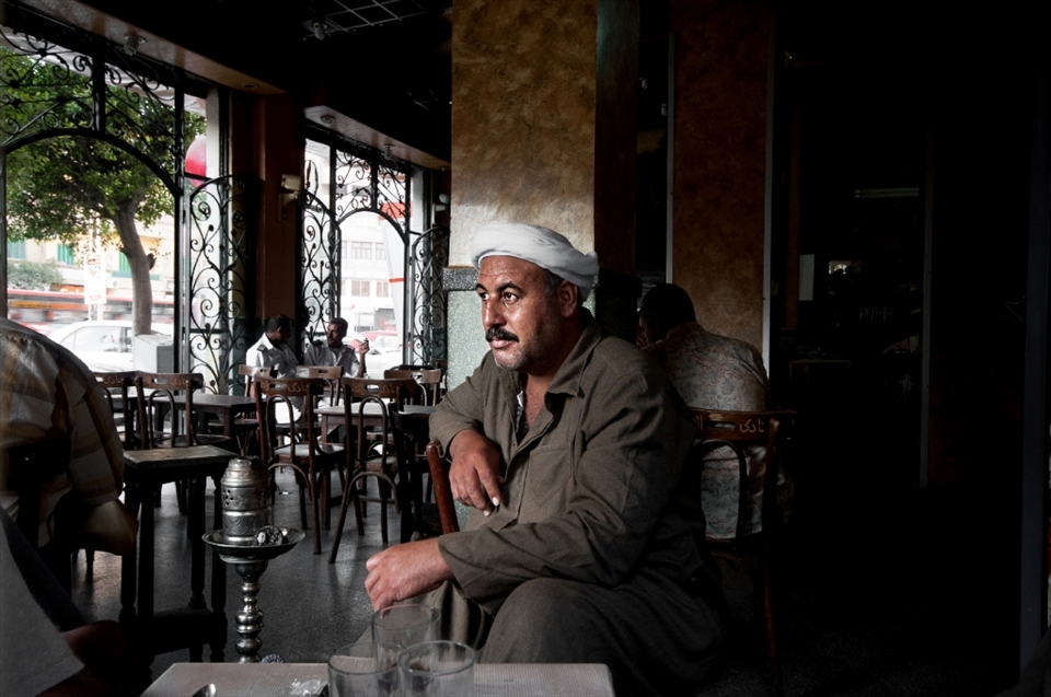 A portrait of a local man who dressed in the traditional Egyptian clothes. he was sitting in a coffe shop at the early morning to have breakfast and smoke some shisha, while other people chatting together at the background(left)
