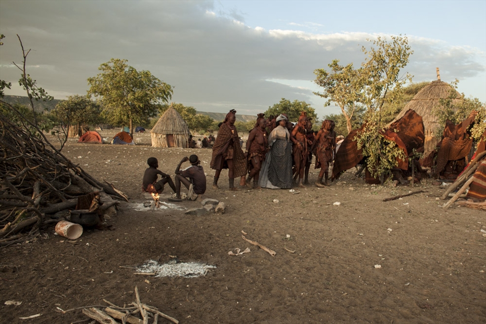 A Herero woman is joining her friends in mourning in a Himba village, while men guard the sacred fire.