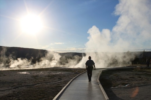 Yellowstone National Park, Wyoming. A man walks into geyser steam as the sun prepares to disappear behind the hill tops