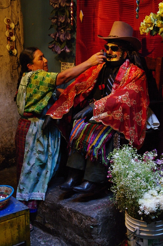 A wooden Maximon is offered a smoke from a wooden pipe as incentive to answer locals' prayers.