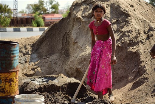 The young girl is doing a man's work, due to the lack of working force in their village. She is helping the women and the remaining men to build a wall around the houses.