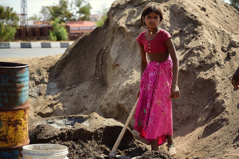 The young girl is doing a man's work, due to the lack of working force in their village. She is helping the women and the remaining men to build a wall around the houses.