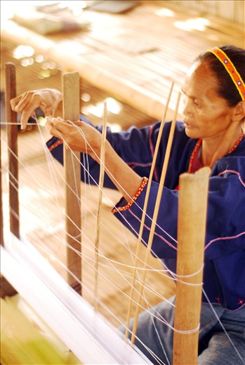 Baye Omeng sets the cotton fibers as the warp on the loom that has been passed down for generations. She relays that they consider this loom to be one of their prized possessions. 