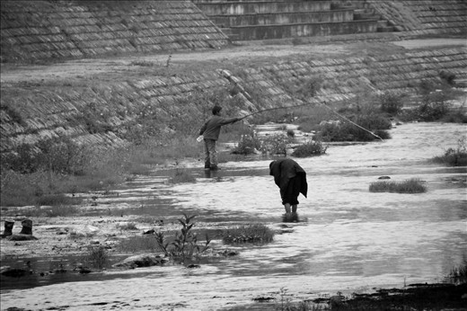 The two people fish in the fish-poor water just meters away from food festival.