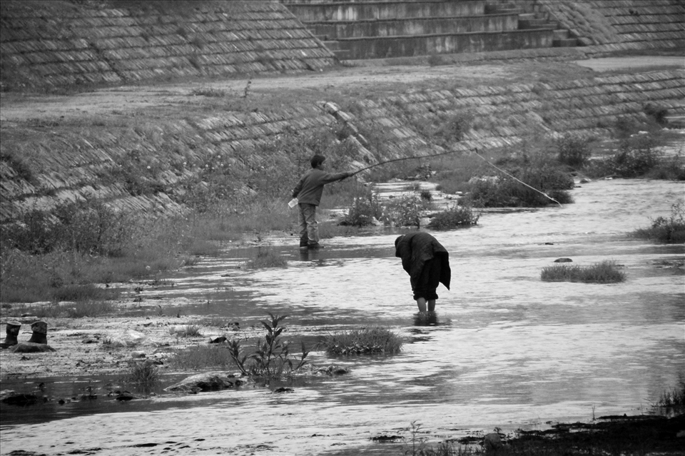 The two people fish in the fish-poor water just meters away from food festival.