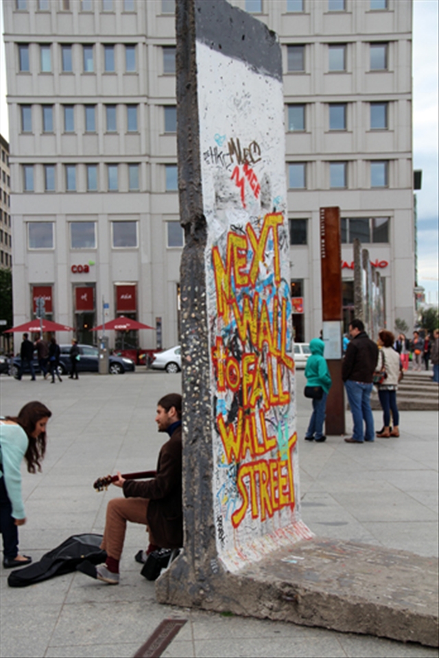 A street musician performs up against a piece of the fallen Berlin Wall.